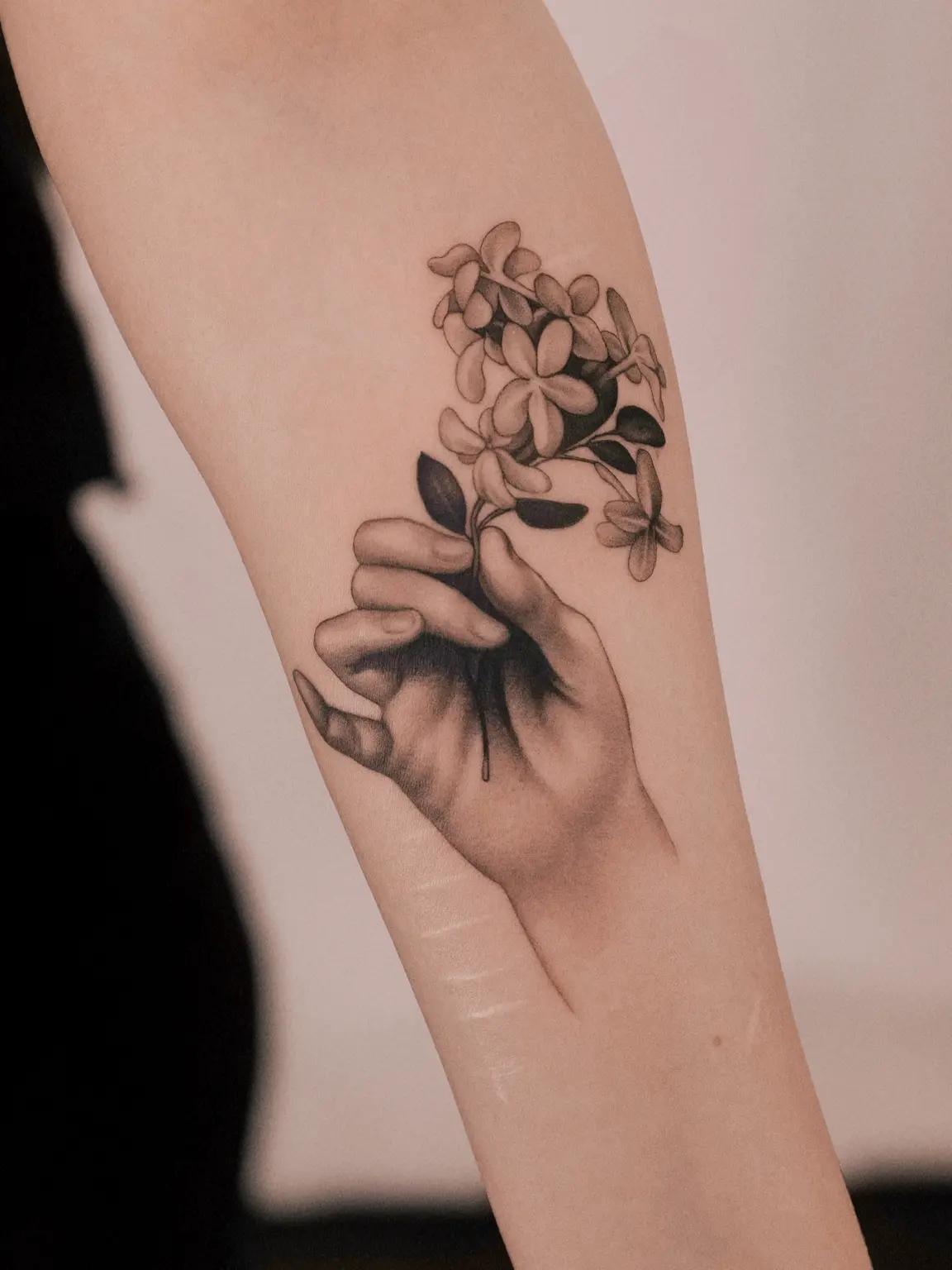 Microrealistic hand holding flowers tattoo